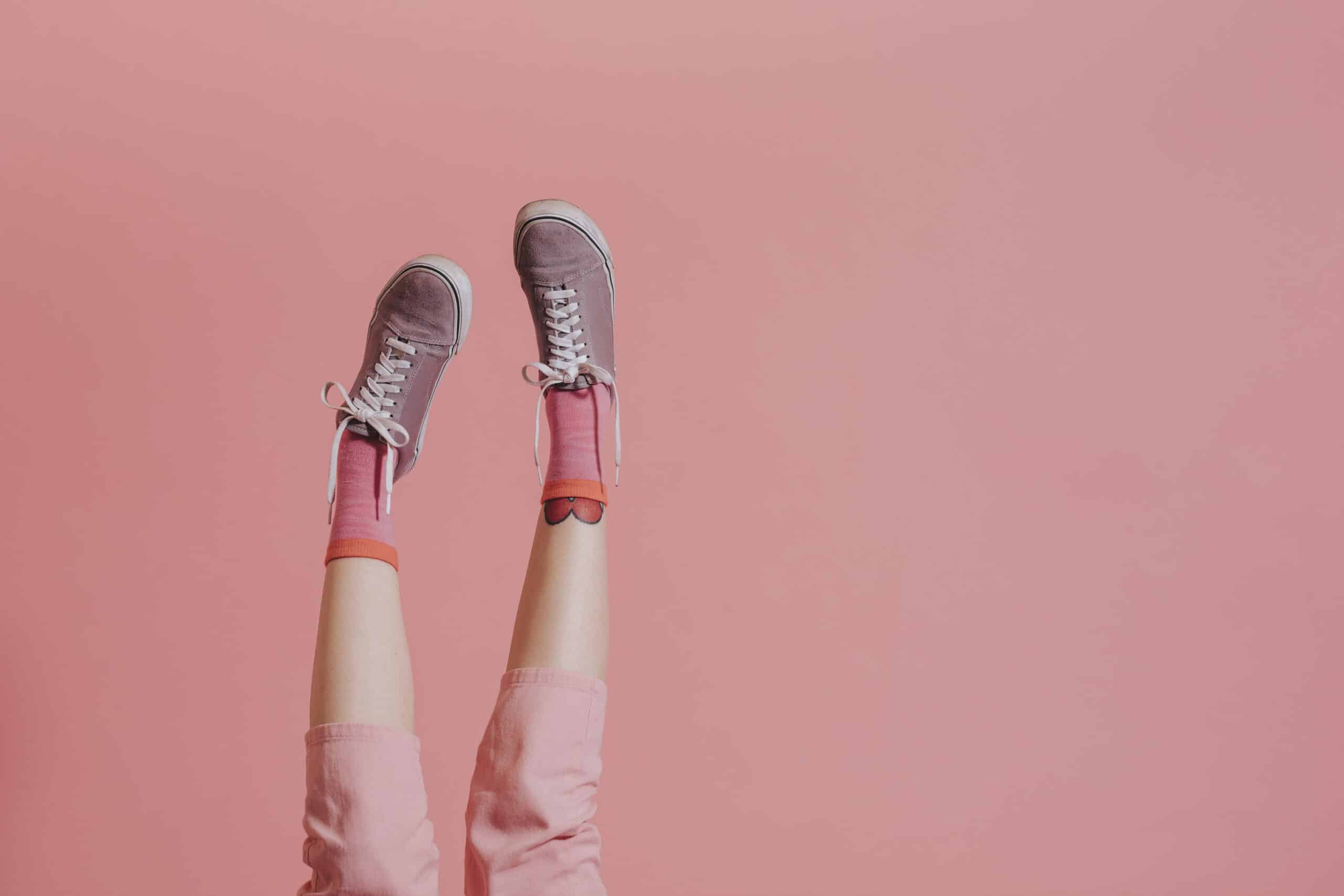 Piernas sobre fondo rosa con pantalon, zapatillas y calcetines rosas