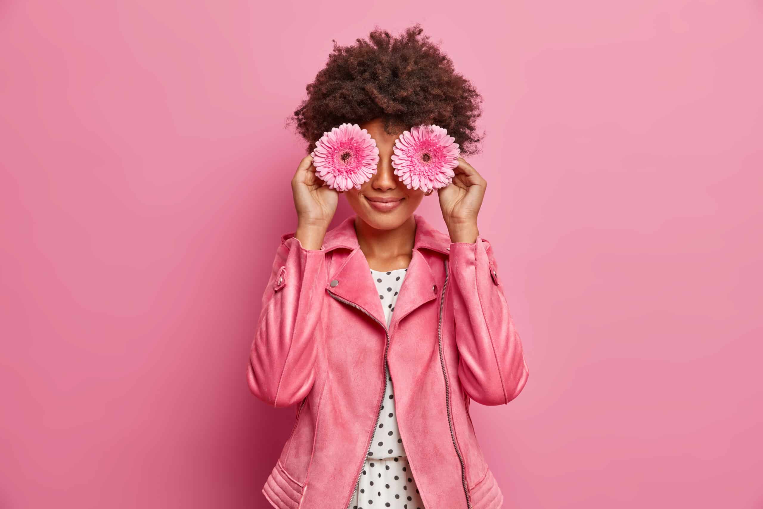 Mujer con chaqueta de cuero rosa con dos flores rosas con las que se tapa los ojos